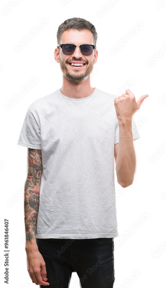 Young tattooed adult man wearing sunglasses pointing and showing with thumb up to the side with happy face smiling Young tattooed adult man wearing sunglasses pointing and showing with thumb up to the side with happy face smiling