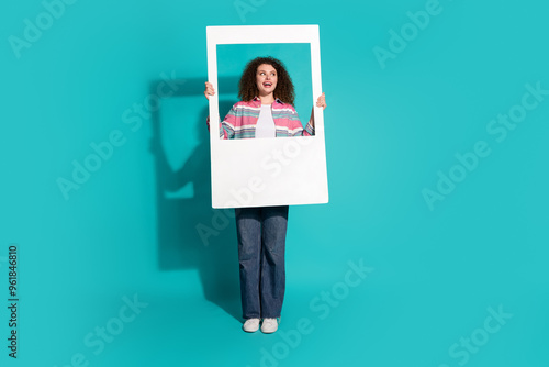 Photo of curly hair funky young brunette lady in striped shirt holding frame window looking novelty isolated on aquamarine color background