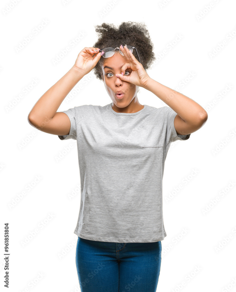 Young afro american woman wearing glasses over isolated background doing ok gesture shocked with surprised face, eye looking through fingers. Unbelieving expression.