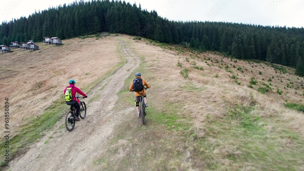 Two cyclists men riding electric bikes outdoors. Back view of male tourists biking in the mountains, wearing helmets and backpacks. Concept of sport, active leisure and nature.