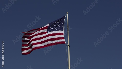 The US flag fluttering in the wind against a blue sky. 4k slo-mo video