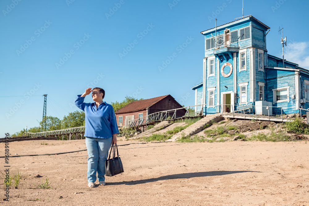 An elderly woman stands at an old river pier.