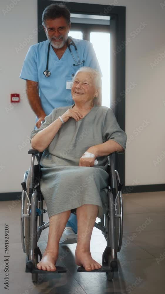 Vertical shot of elderly male doctor or caregiver pushing old female patient in a wheelchair in hospital for healthcare help. Vertical shot of elderly male doctor or caregiver pushing old female patient in a wheelchair in hospital for healthcare help.