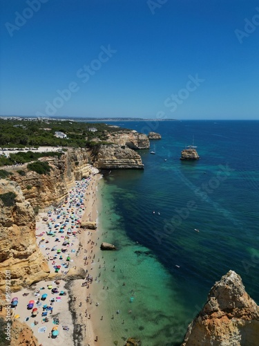 The photo shows the impressive limestone arches near Benagil Cave in the Algarve, Portugal. Crystal-clear green waters flow beneath the towering cliffs, set against a bright blue sky and rugged coastl photo