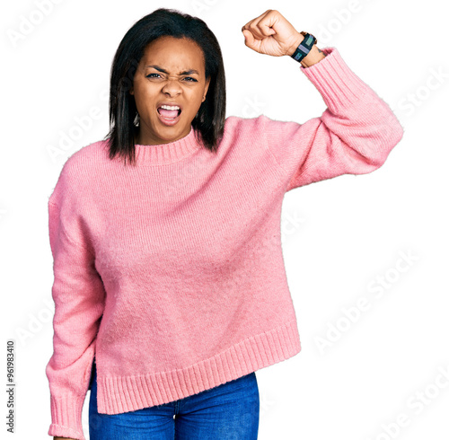 Beautiful hispanic woman wearing casual winter sweater angry and mad raising fist frustrated and furious while shouting with anger. rage and aggressive concept.