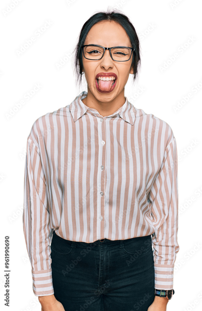 Fototapeta premium Young hispanic girl wearing casual clothes and glasses sticking tongue out happy with funny expression. emotion concept.