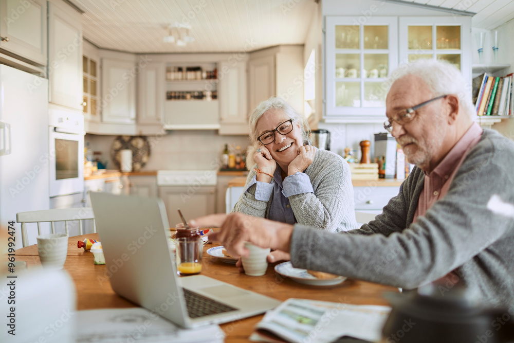 Elderly couple having breakfast and using a laptop in the kitchen Elderly couple having breakfast and using a laptop in the kitchen