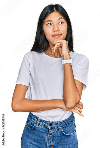 Beautiful young asian woman wearing casual white t shirt with hand on chin thinking about question, pensive expression. smiling and thoughtful face. doubt concept.