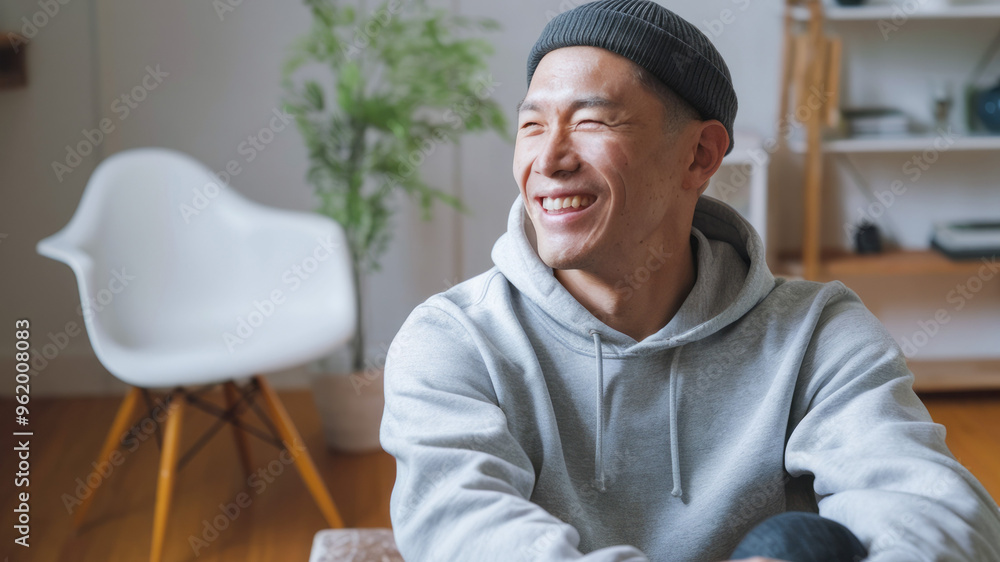 Fototapeta premium Happy man in hoodie. Man in gray hoodie, smiling, looking away, sitting on a couch.