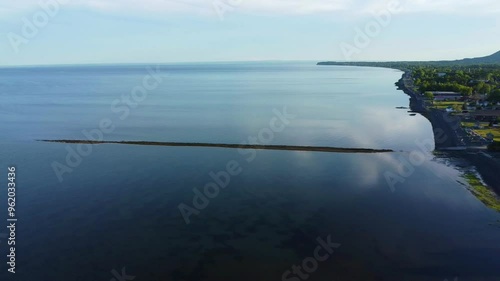 Les vestiges d'un ancien quai traverse une immense baie à l'eau calme réfletant le bleu du ciel sur le littoral  d'un village côtier aux habitations parsemées. ( Maria, Gaspésie, Baie-des-Chaleurs ) photo