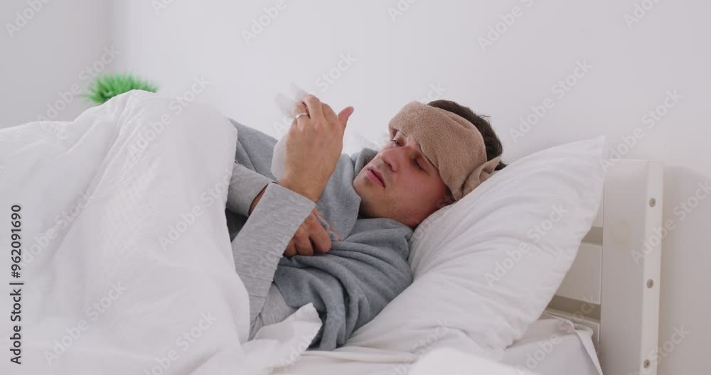Sick young man lying on bed in bedroom under white blanket suffering from runny nose and temperature at home. Guy with flu or cold feeling unhealthy with influenza. 4k video. Slow motion video. Sick young man lying on bed in bedroom under white blanket suffering from runny nose and temperature at home. Guy with flu or cold feeling unhealthy with influenza. 4k video. Slow motion video.