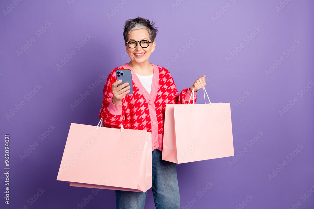 Photo portrait of cute senior woman hold device shopping bags dressed stylish red clothes isolated on violet color background Photo portrait of cute senior woman hold device shopping bags dressed stylish red clothes isolated on violet color background