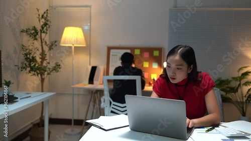 Two busy colleagues working together talking using laptop in office. Middle aged Asian fem, male worker looking at computer discussing business plan at office meeting. photo