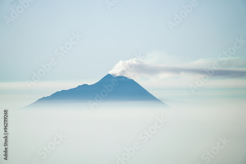 Mount Merapi volcano emitting smoke from its crater seen afar from Mount Prau with blue sky and white clouds in Dieng, Wonosobo, Indonesia. photo