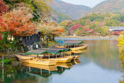 View of colorful maple leaves in autumn season at Arashiyama and Katsura river from Togetsu or Togetsukyo bridge. Boats for tourists to enjoy autumn view. Destination of Kyoto, Japan photo