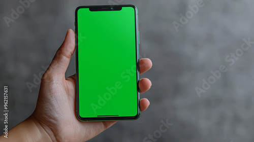 A hand holds up a smartphone with a green screen.