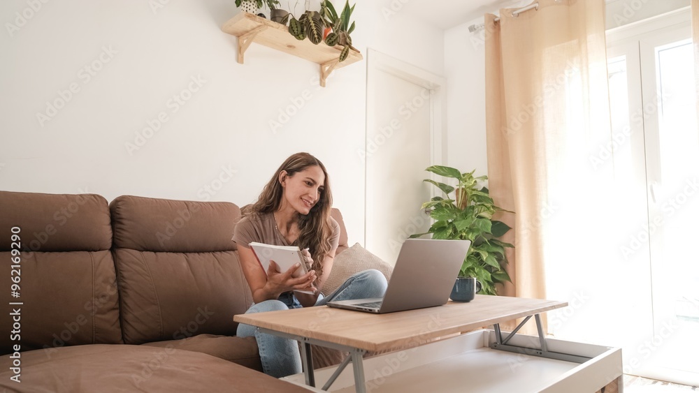 Happy woman writing in diary while working on laptop at home Happy woman writing in diary while working on laptop at home