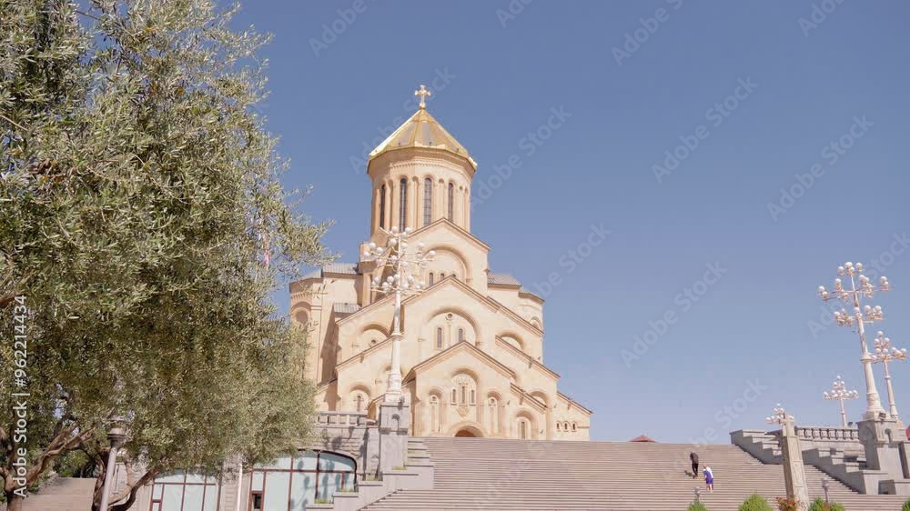 Tourists climbing steps leading to holy trinity cathedral of tbilisi, georgia on sunny day, with bright blue sky in background Tourists climbing steps leading to holy trinity cathedral of tbilisi, georgia on sunny day, with bright blue sky in background