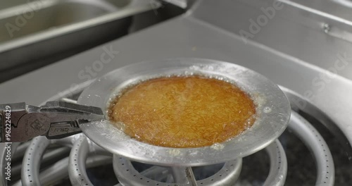 Pastry chef prepares traditional Turkish kunefe or kanafeh with pistachio on a stove. Boiling sugar syrup in a copper plate photo