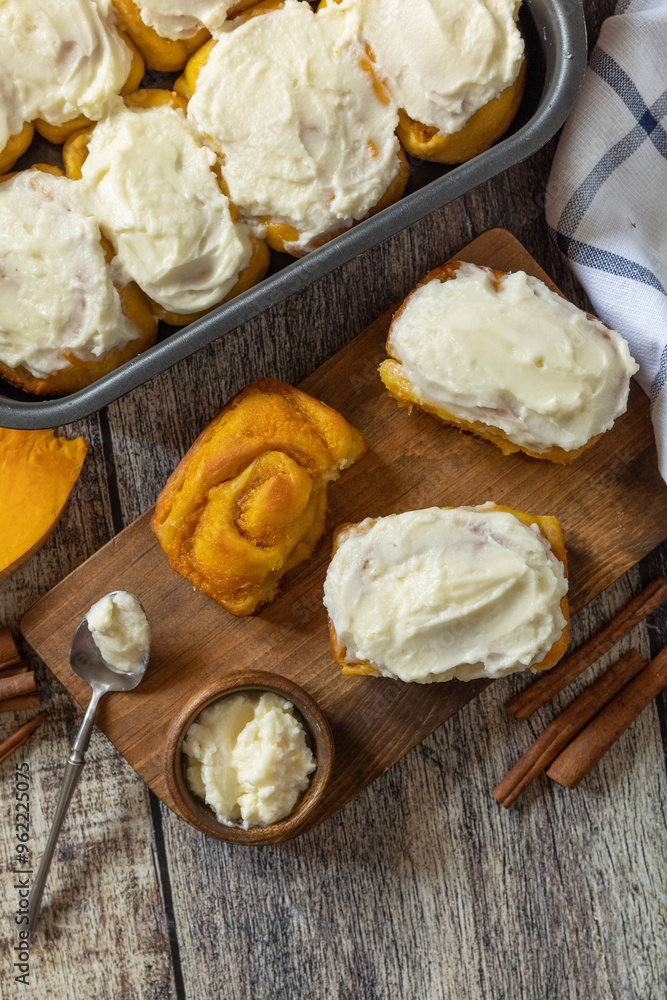 Freshly baked pumpkin cinnamon rolls or cinnabon with cream cheese on a rustic wooden table. Homemade seasonal autumn homemade pastry. Freshly baked pumpkin cinnamon rolls or cinnabon with cream cheese on a rustic wooden table. Homemade seasonal autumn homemade pastry.