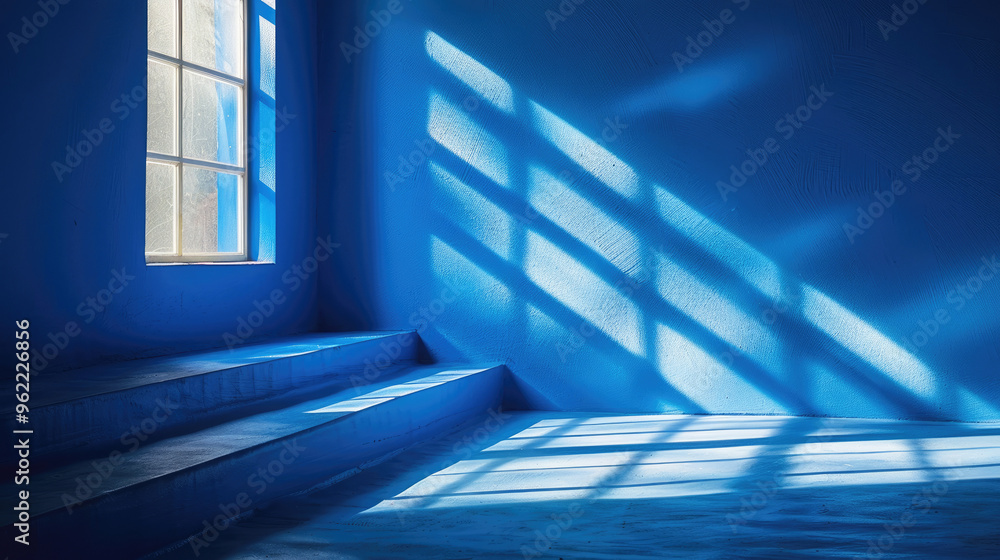 Obraz premium Empty blue room. Sunlight streams through a grid window, casting soft, geometric shadows on a textured blue wall and floor. 