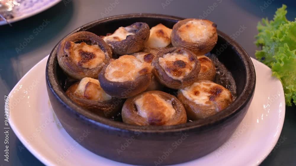 Plate of baked mushrooms topped with melted cheese slowly rotates, showing off alluring look of this delicious appetizer. Oil boils in plate. Hot dish. Plate of baked mushrooms topped with melted cheese slowly rotates, showing off alluring look of this delicious appetizer. Oil boils in plate. Hot dish.