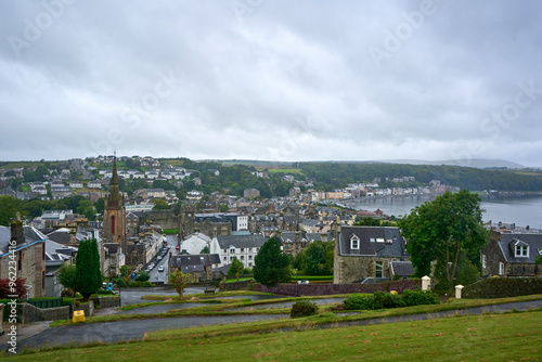 A picturesque town with a meandering road by water, blending urban and rural charm. Vibrant nature contrasts the peaceful urban setting for an idyllic countryside scene.