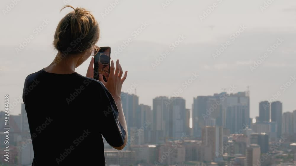 Young woman taking photos with smartphone of vast cityscape. It stands on top of hill overlooking entire city of Batumi in Georgia. Young woman taking photos with smartphone of vast cityscape. It stands on top of hill overlooking entire city of Batumi in Georgia.