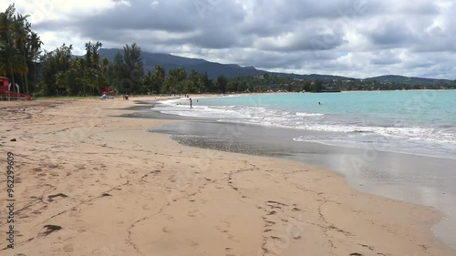 water crashing on shore on beautiful beach in luquillo puerto rico (caribbean sea island travel vacation getaway) idyllic empty popular hotel tourism el yunque waves surf sand clouds palm trees photo