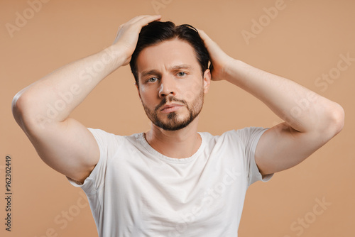 Handsome male model touching hair on beige background looking at camera hair loss problem, treatment