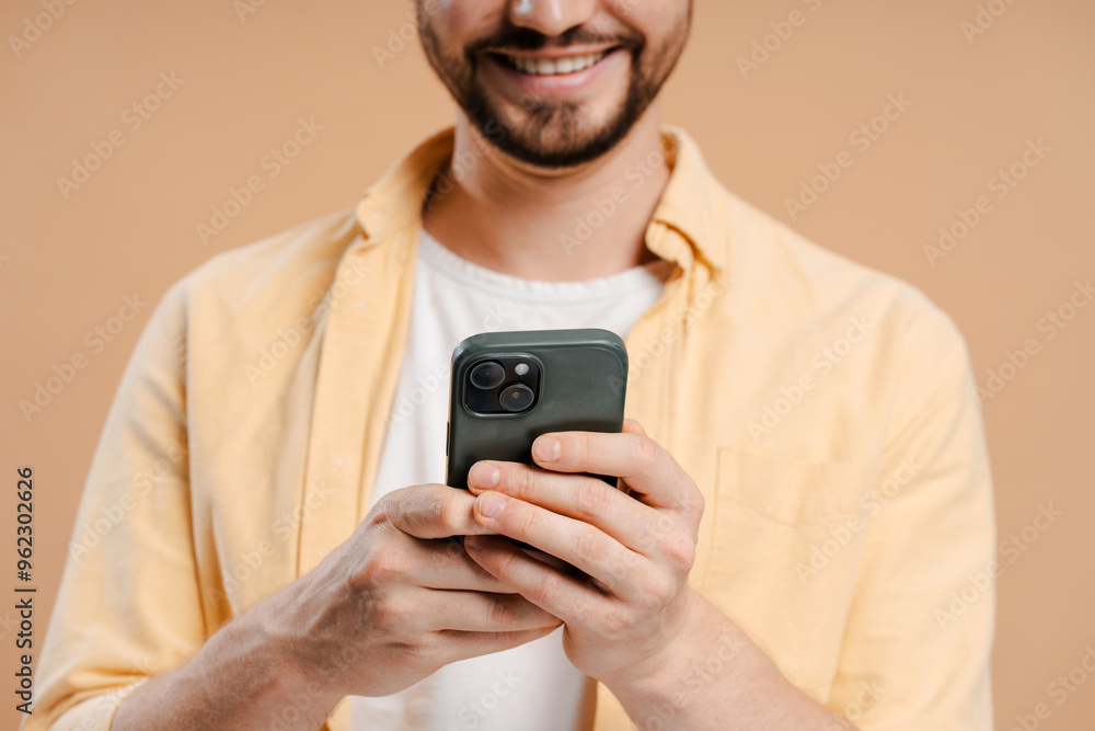 Bearded man holding using smartphone reading good news on social media isolated on beige background Bearded man holding using smartphone reading good news on social media isolated on beige background