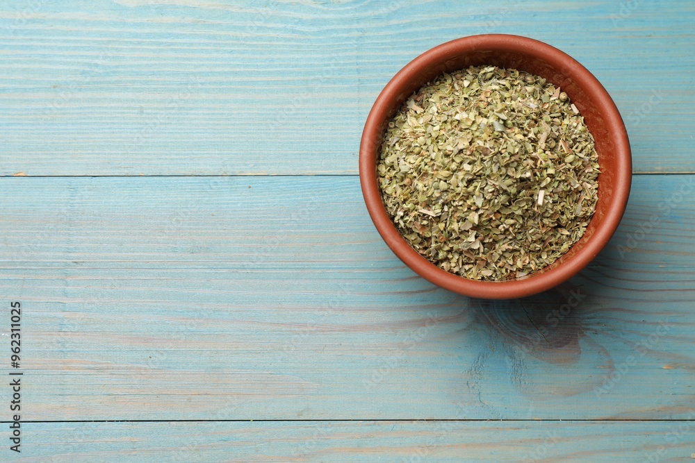 Dried oregano in bowl on light blue wooden table, top view. Space for text Dried oregano in bowl on light blue wooden table, top view. Space for text
