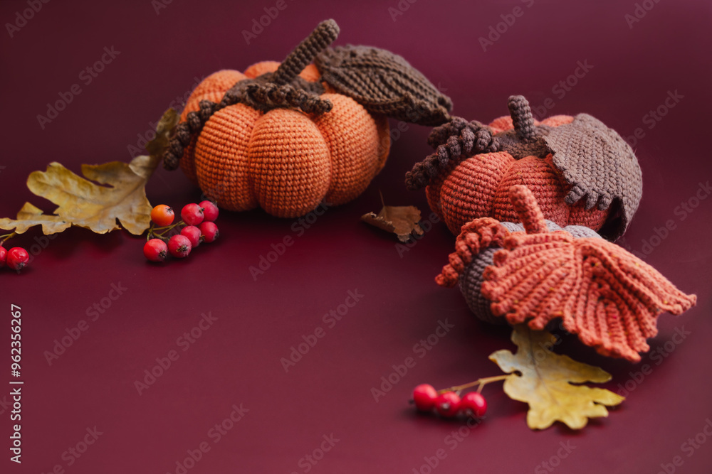 Naklejka premium Knitted pumpkins top view. Knitted autumn decor on dark red background with fall leaves and berries. Copy space