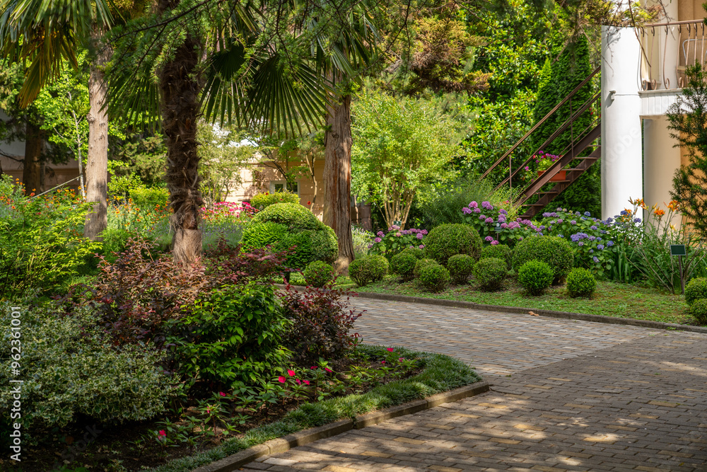 Fototapeta premium A beautiful pathway meanders through a vibrant garden filled with colorful flowers and perfectly trimmed shrubs under bright daylight