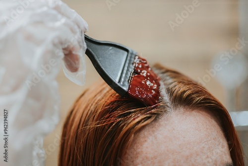 woman applying hair dye with a special brush wearing gloves at home in the bathroom