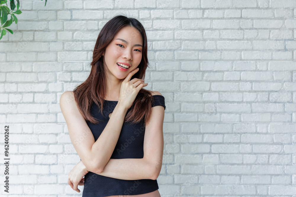 Smiling Young Woman Posing Casually in Black Top Against White Brick Wall Smiling Young Woman Posing Casually in Black Top Against White Brick Wall