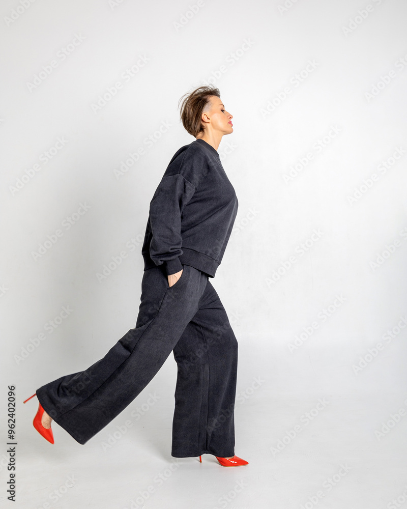 Portrait beautiful woman of model appearance. Girl in black jumper and trousers, red shoes on grey background. Pretty female with trendy makeup posing in studio. Vertical photo. High quality photo Portrait beautiful woman of model appearance. Girl in black jumper and trousers, red shoes on grey background. Pretty female with trendy makeup posing in studio. Vertical photo. High quality photo