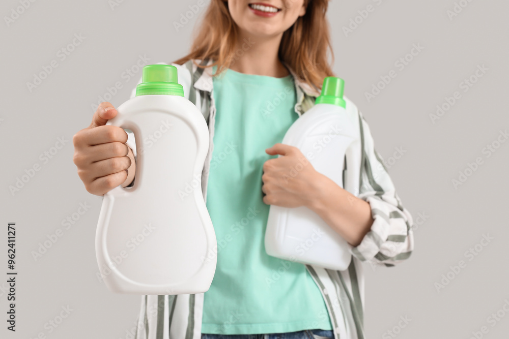 Young woman with bottles of laundry detergent on grey background Young woman with bottles of laundry detergent on grey background