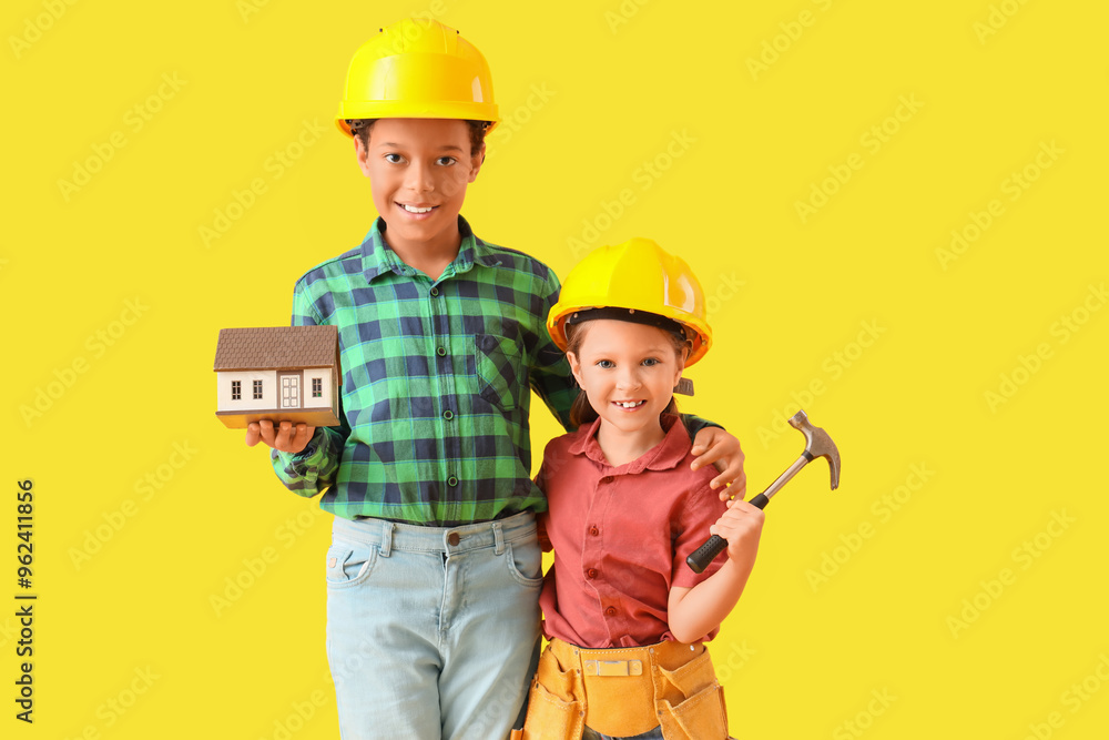 Cute little architects with house model and hammer on yellow background Cute little architects with house model and hammer on yellow background