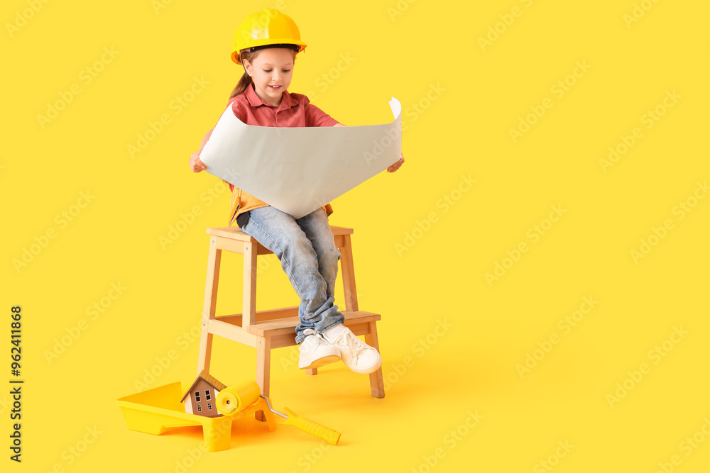 Cute little architect sitting on stepladder and reading blueprint against yellow background Cute little architect sitting on stepladder and reading blueprint against yellow background