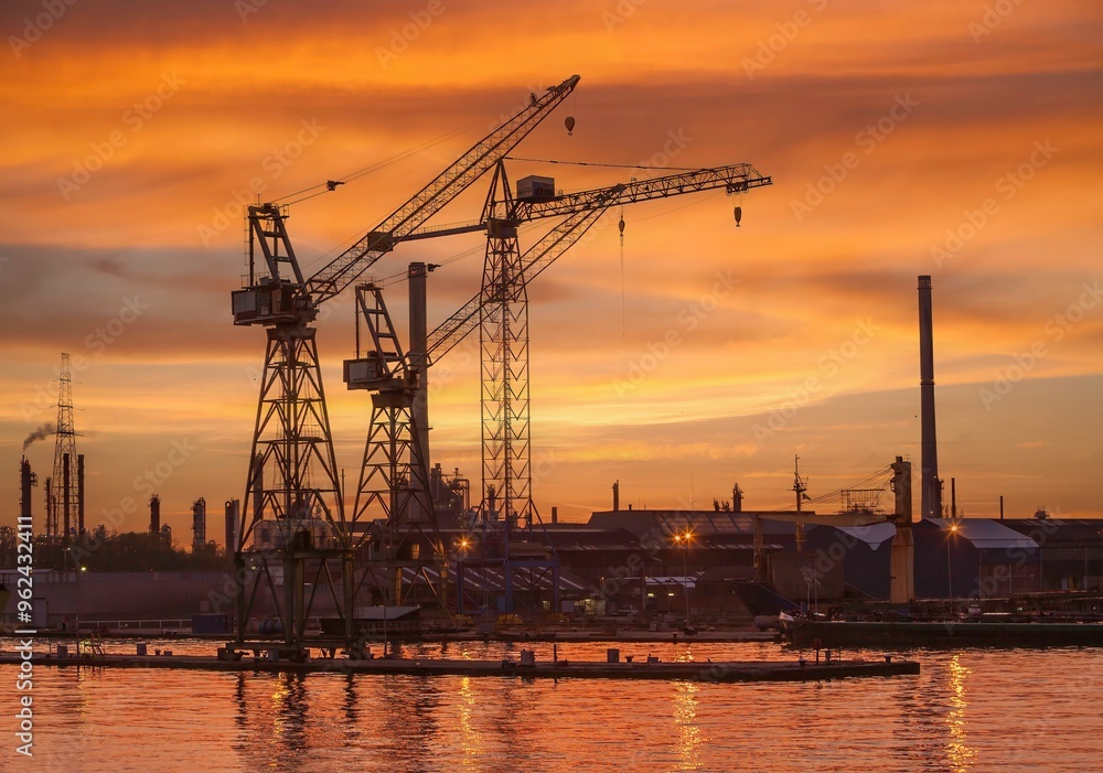 Tower cranes and elements of an oil refinery are silhouetted against a brilliant sunset near Antwerpn, Belgium. Tower cranes and elements of an oil refinery are silhouetted against a brilliant sunset near Antwerpn, Belgium.