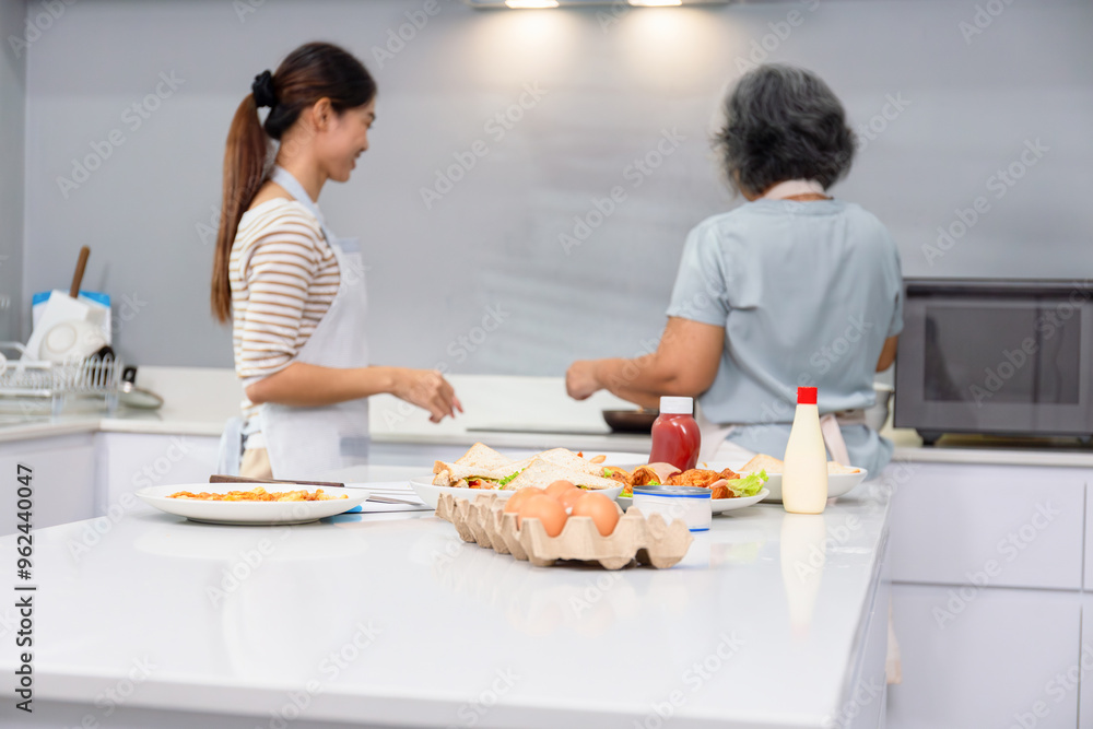 Selective focus on food on table, Senior asian mother and middle aged daughter cooking together at kitchen Selective focus on food on table, Senior asian mother and middle aged daughter cooking together at kitchen