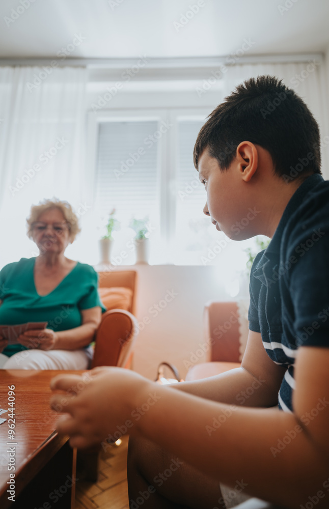 A senior woman and young boy are sitting together playing cards in a cozy living room, fostering family bonding and leisure time. A senior woman and young boy are sitting together playing cards in a cozy living room, fostering family bonding and leisure time.