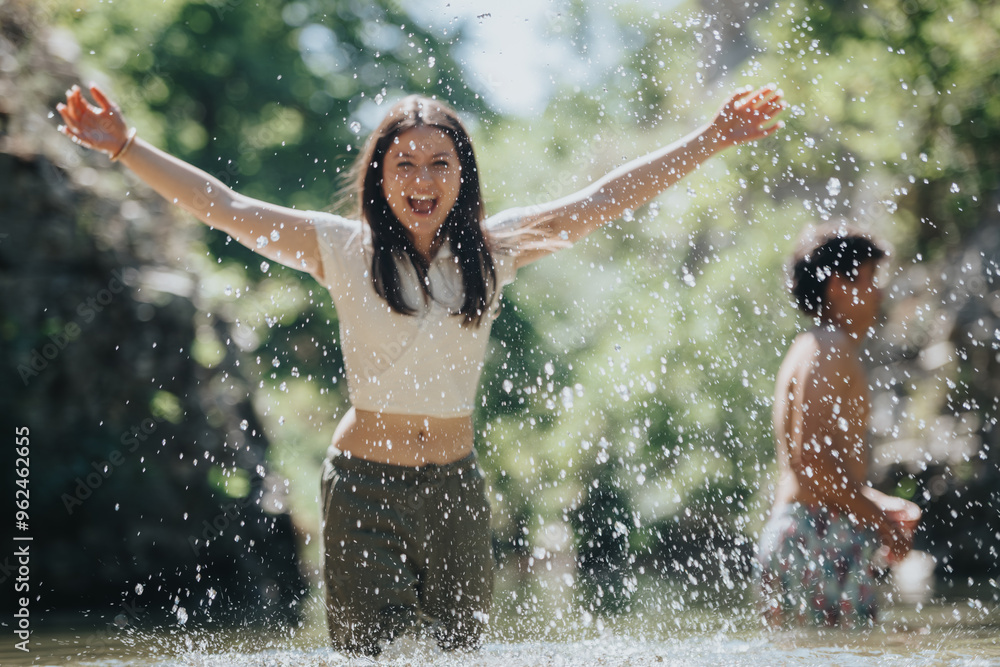 Fototapeta premium Happy young individuals having fun splashing in a natural water setting on a sunny day. Carefree energy and joy in a vibrant outdoor environment.