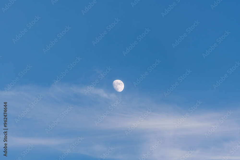 A serene moon captured in a blue daytime sky with soft clouds, conveying calm and peace. A serene moon captured in a blue daytime sky with soft clouds, conveying calm and peace.