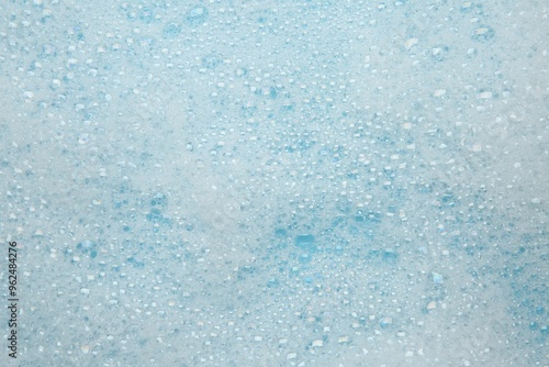 Washing laundry. White foam with bubbles on light blue background, top view