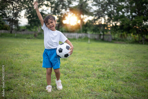 A young girl is holding a soccer ball in a park. She is smiling and she is enjoying herself