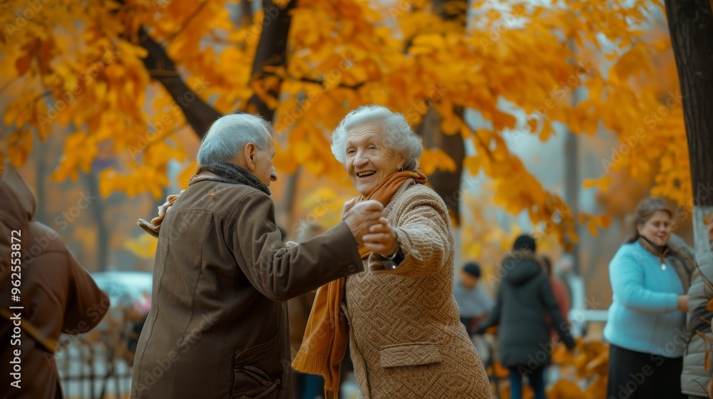 An elderly couple dances happily in a park adorned with golden autumn leaves. The man, in a brown coat, leads his smiling partner, dressed in a beige coat, in a lively dance, surrounded by other An elderly couple dances happily in a park adorned with golden autumn leaves. The man, in a brown coat, leads his smiling partner, dressed in a beige coat, in a lively dance, surrounded by other
