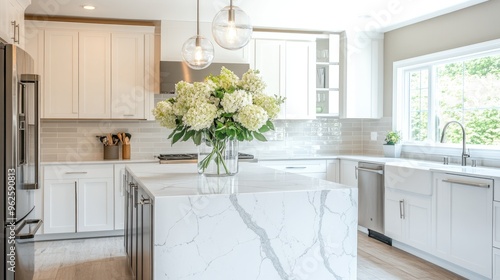An open-concept kitchen with white cabinetry, a sleek marble island, and stainless steel appliances, complemented by fresh flowers in a glass vase.