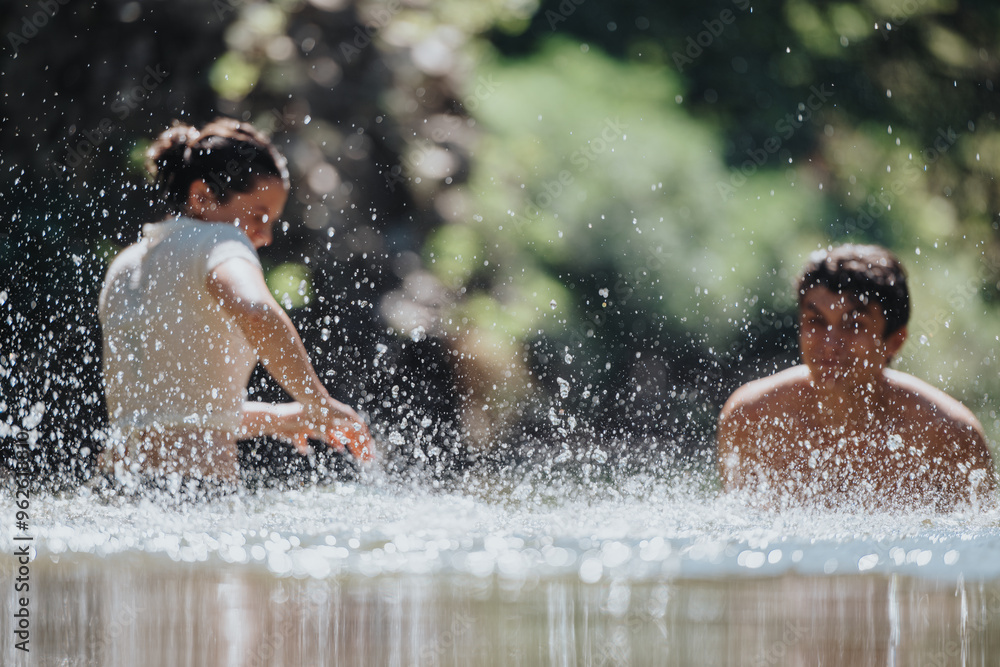 Fototapeta premium Two young adults enjoy a playful moment in water, splashing and laughing under the warm sun in nature.